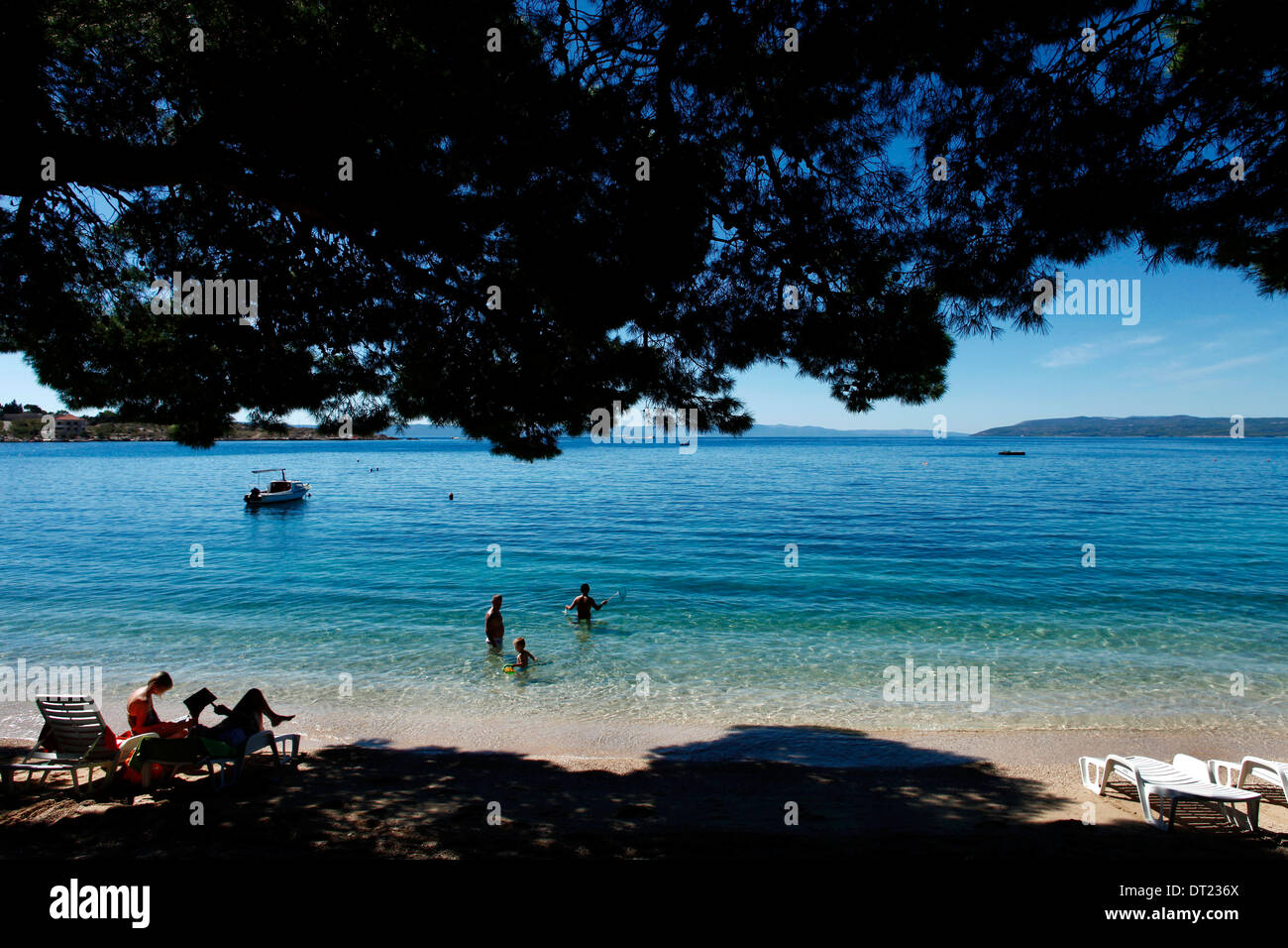 Mare in una giornata di sole con alcuni alberi creando ombre sulla linea di galleggiamento e alcune persone nuoto Foto Stock