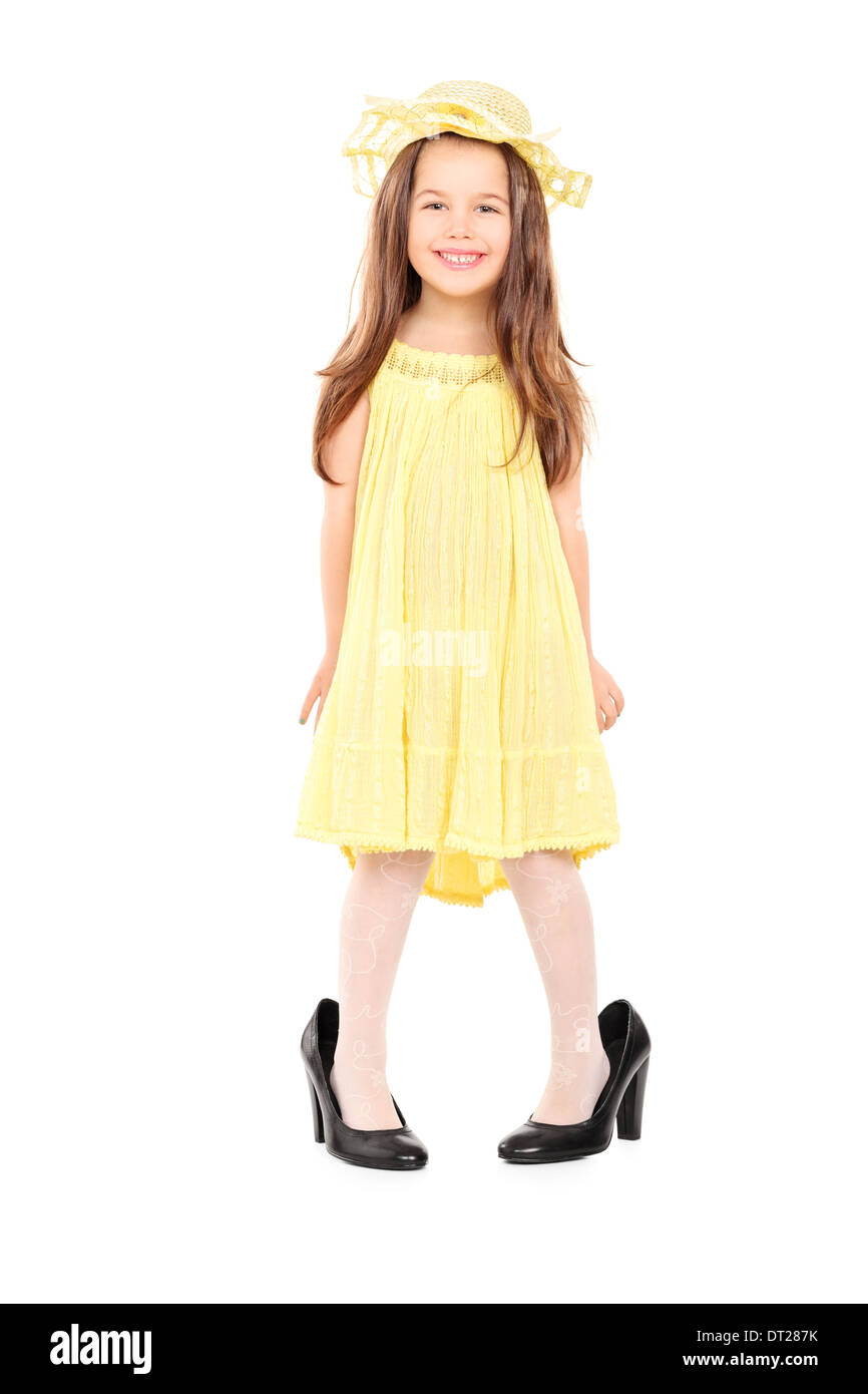 A piena lunghezza Ritratto di adorabile bambina in fantasia abito giallo e hat in piedi in grandi tacchi alti Foto Stock