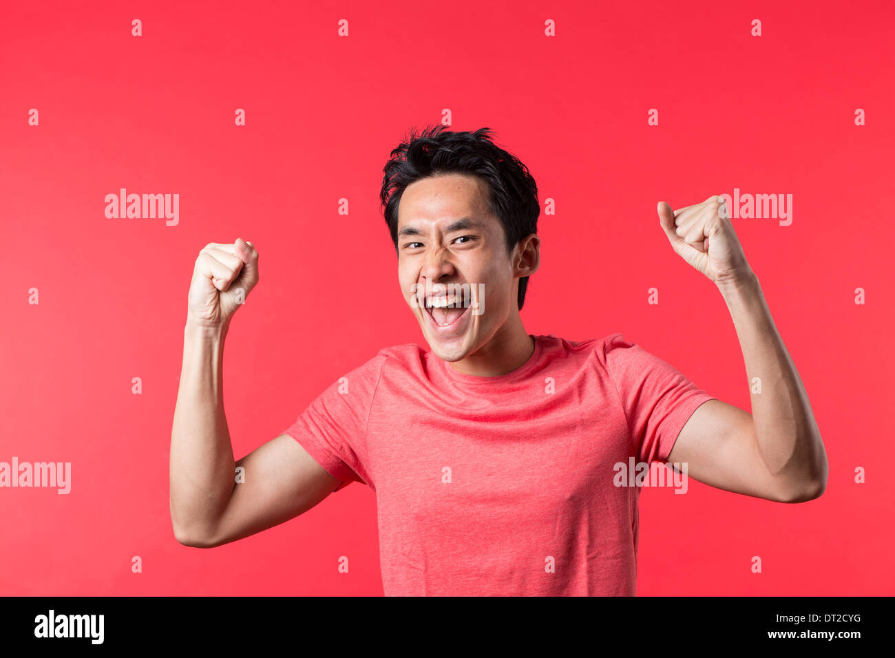 Allegro uomo asiatico celebrando con il suo braccio verso l'alto. Di fronte a sfondo rosso Foto Stock