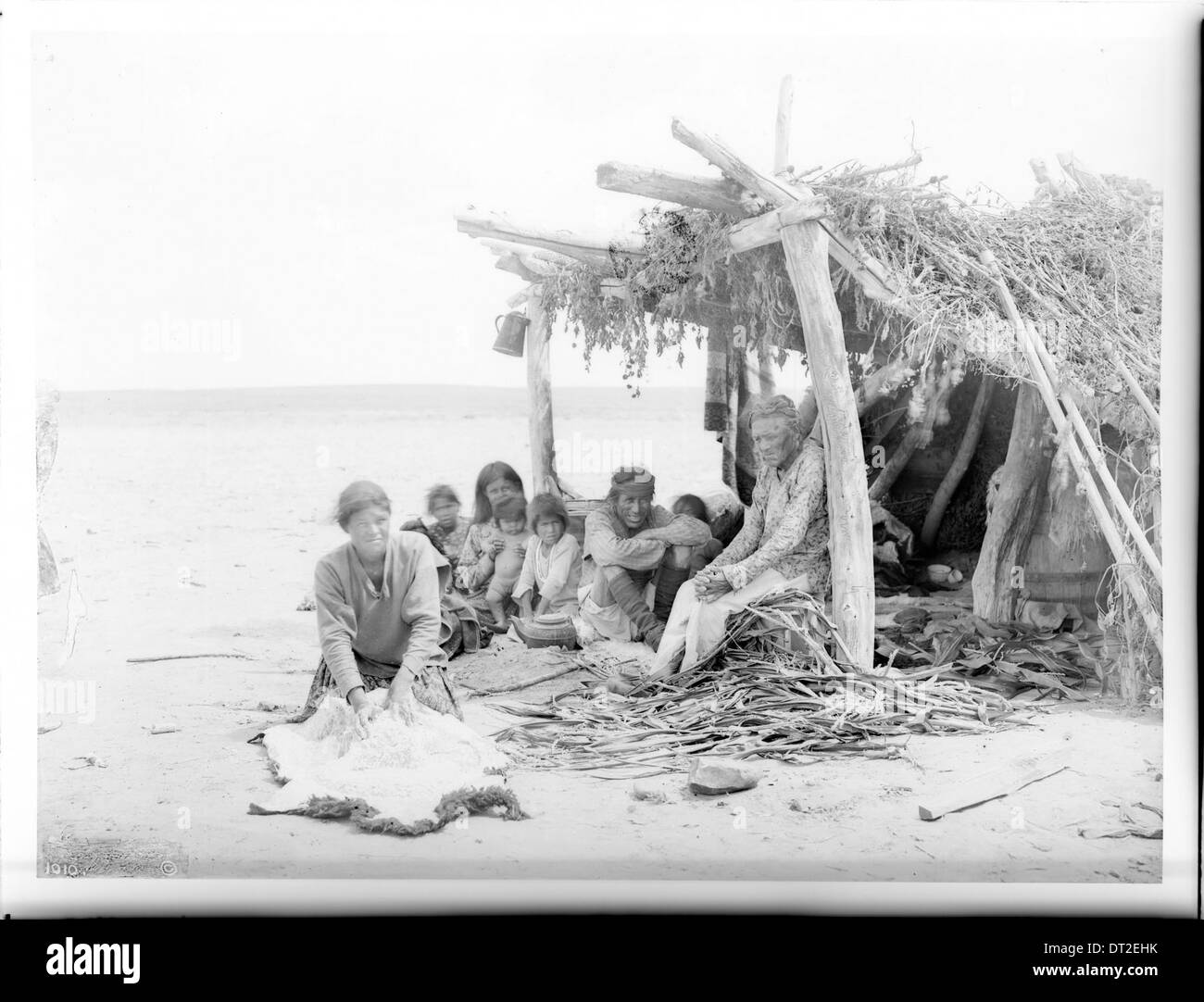 Una famiglia Navajo viene vista all'interno della loro hogan sul deserto dipinto, preparando un pasto. La foto offre una vista laterale della famiglia impegnata nelle attività quotidiane. Foto Stock