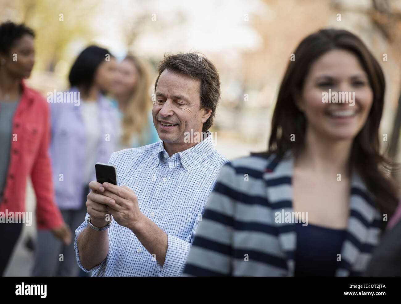 La gente all'aperto nella città in primavera tempo un uomo controllando il suo telefono cellulare tra Foto Stock