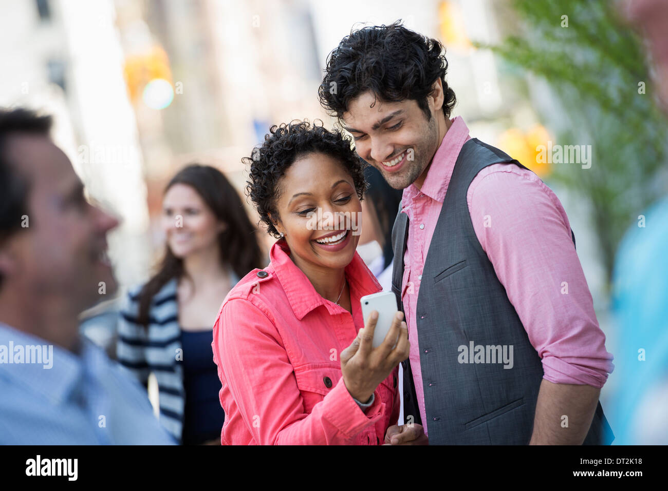 La gente all'aperto in primavera tempo New York City Park quattro persone uomini e donne una coppia in cerca di un telefono cellulare schermo Foto Stock