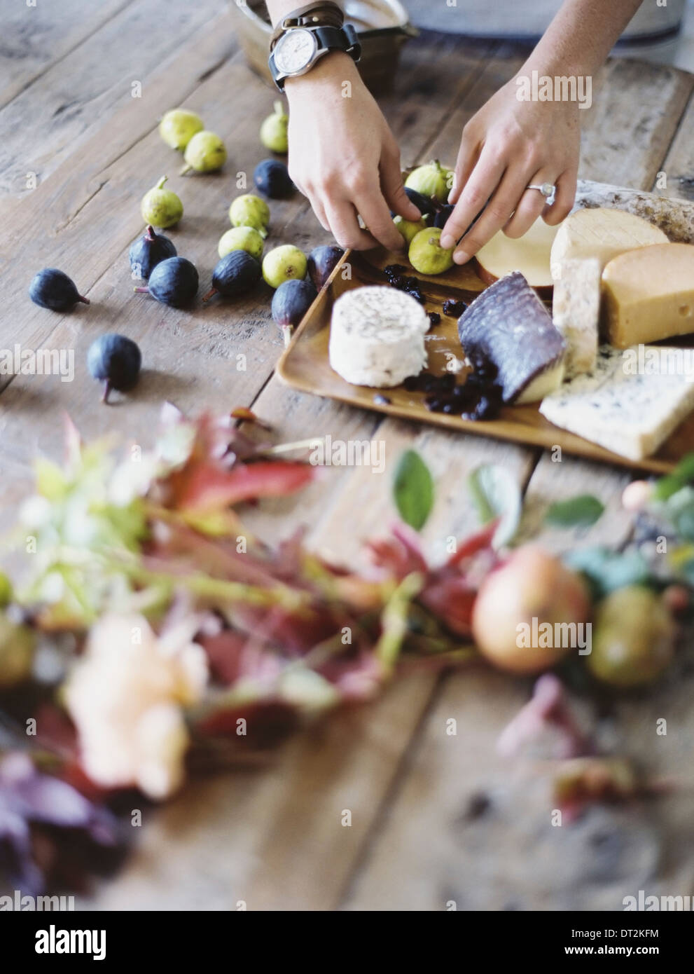 Una donna alla cucina domestica tabella disponendo la frutta fresca verde e nero le figure su un vassoio di formaggi cibo organico dalla fattoria alla piastra Foto Stock