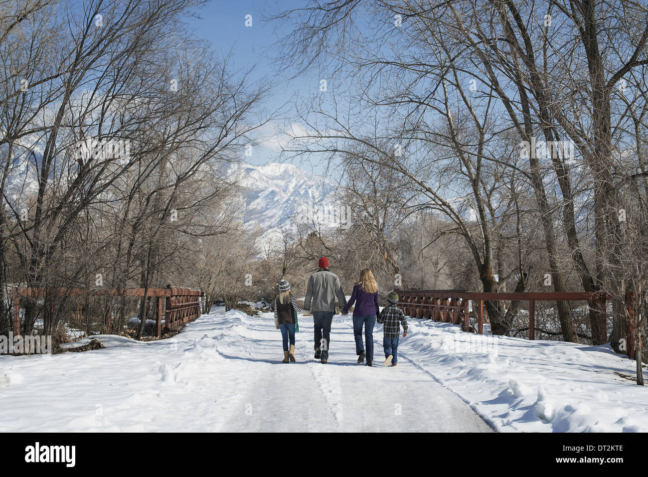 Paesaggio invernale con neve sul terreno una famiglia adulti e due bambini a piedi giù per una strada vuota Foto Stock