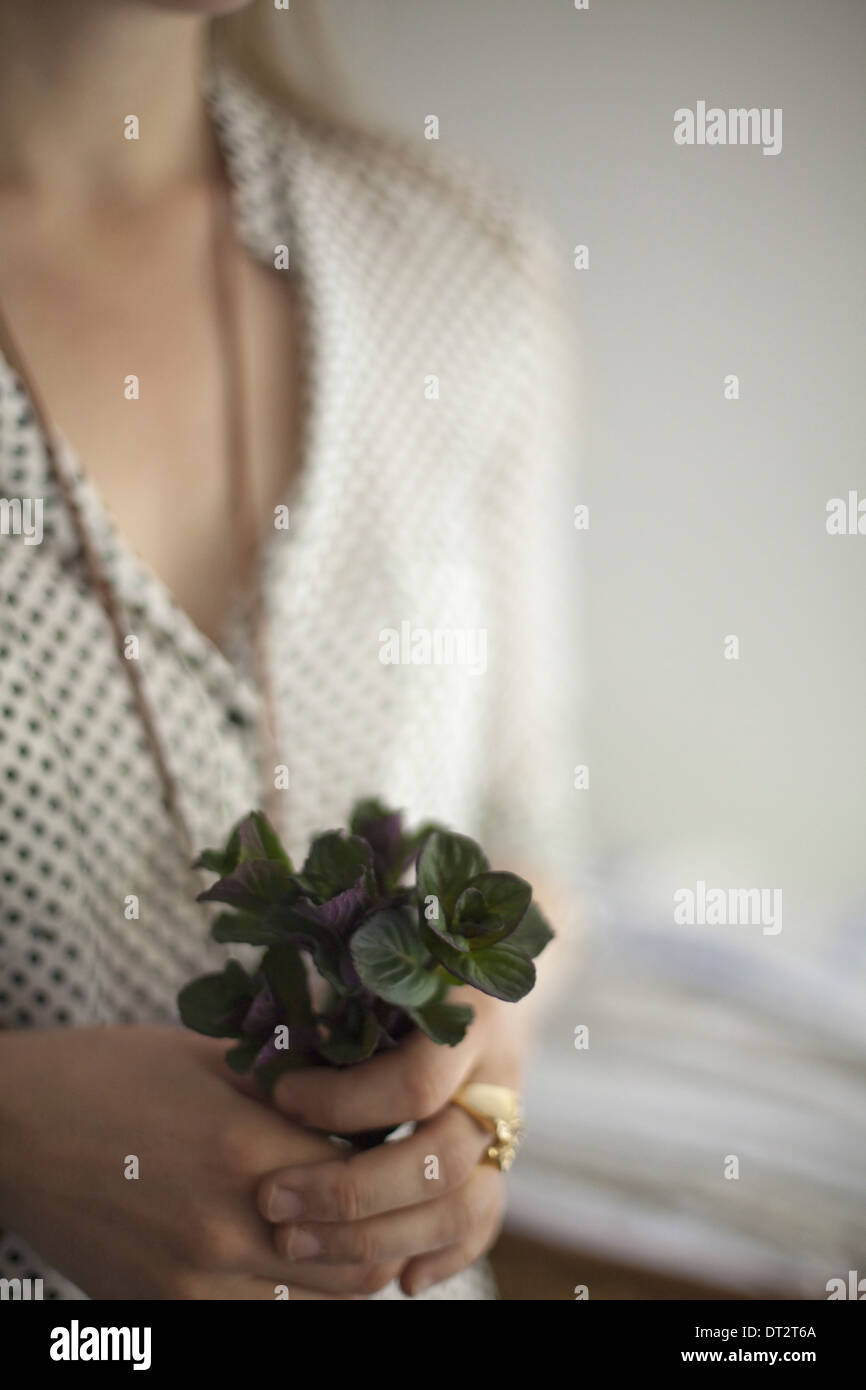 Una donna che indossa un abito e collana tenendo un mazzetto di colore rosso e verde foglie di piante di Colonia con foglie di menta Foto Stock