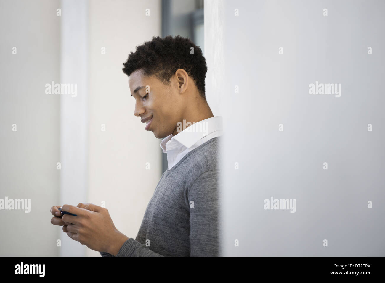 Un giovane uomo in un maglione grigio utilizzando il suo telefono cellulare Foto Stock
