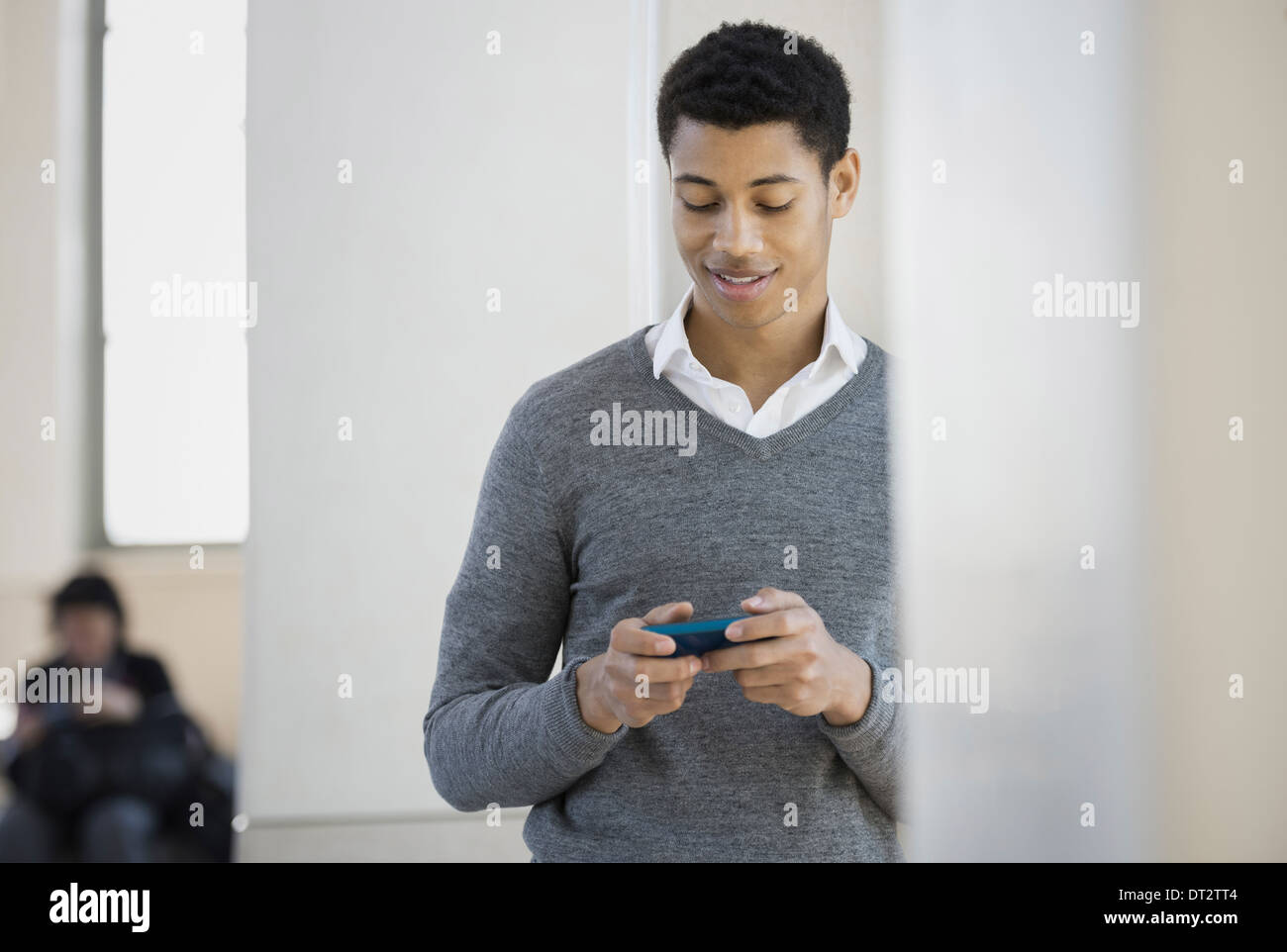 Un giovane uomo in un maglione grigio utilizzando il suo telefono cellulare Foto Stock