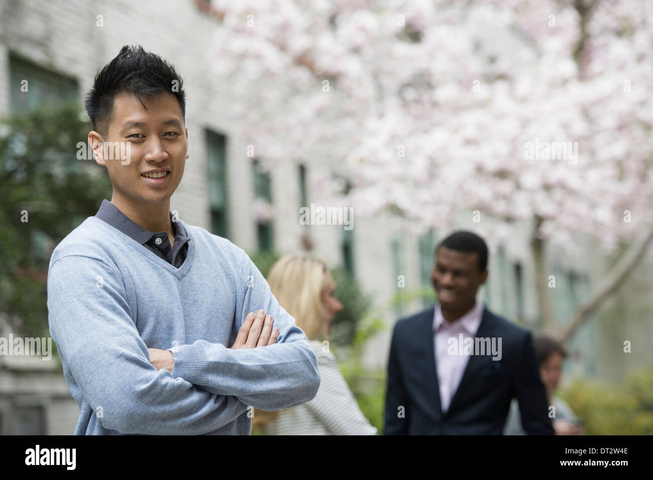 Vista su cityA uomo con le braccia piegate e due persone che parlano in background sotto gli alberi in fiore Foto Stock