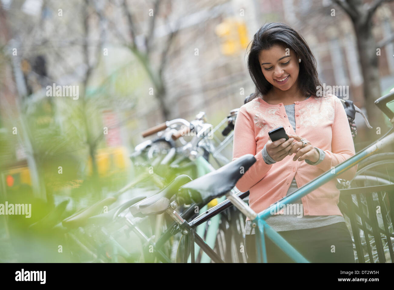 Vista su cityA giovane donna in una pesca shirt colorate con il suo smart phone Biciclette parcheggiate in un portabicicletta Foto Stock