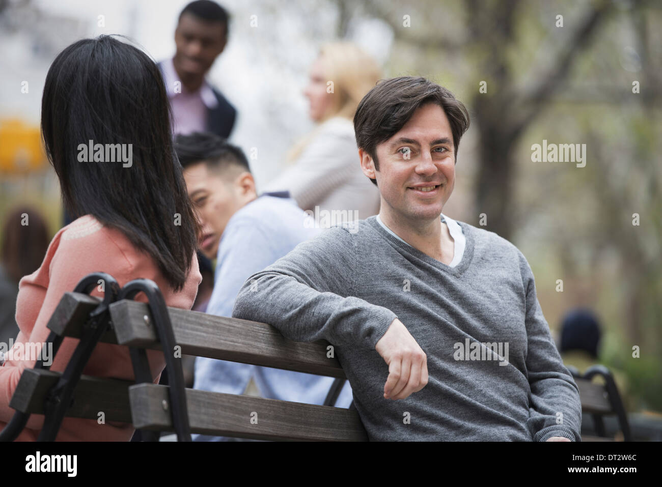Vista su citySitting su una panchina nel parco un uomo sorridente la fotocamera a quattro persone in background Foto Stock