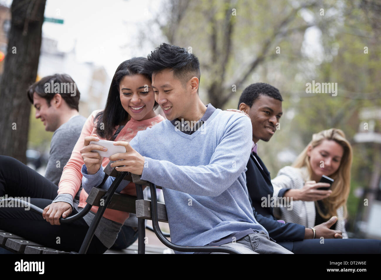 Vista sulla città seduta su una panchina un uomo che mostra la sua schermata telefono per una donna e tre altre persone che controllano i loro telefoni cellulari Foto Stock