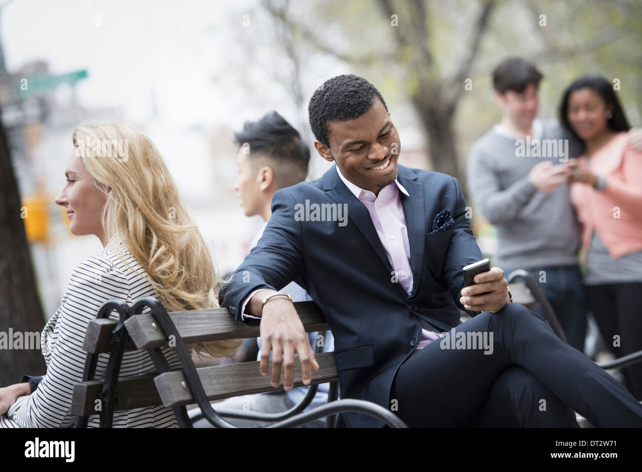 Vista sulla città si radunò intorno a una panchina nel parco due controllando uno smart phone per i messaggi Foto Stock