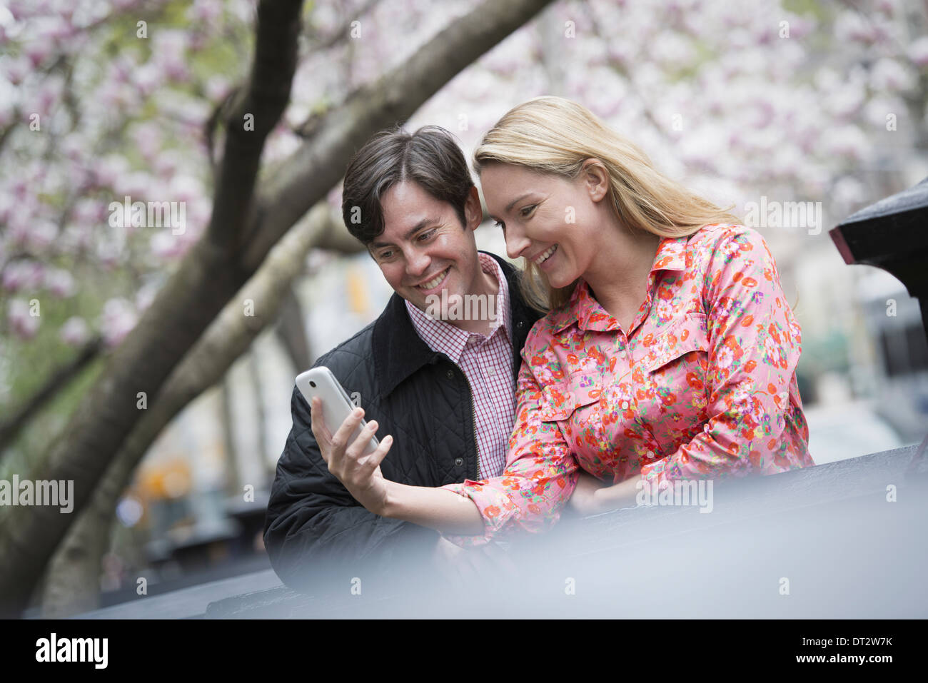 Vista su cityYoung persone parco all'aperto una giovane donna e uomo seduto di fianco a fianco che guarda uno smart phone Foto Stock