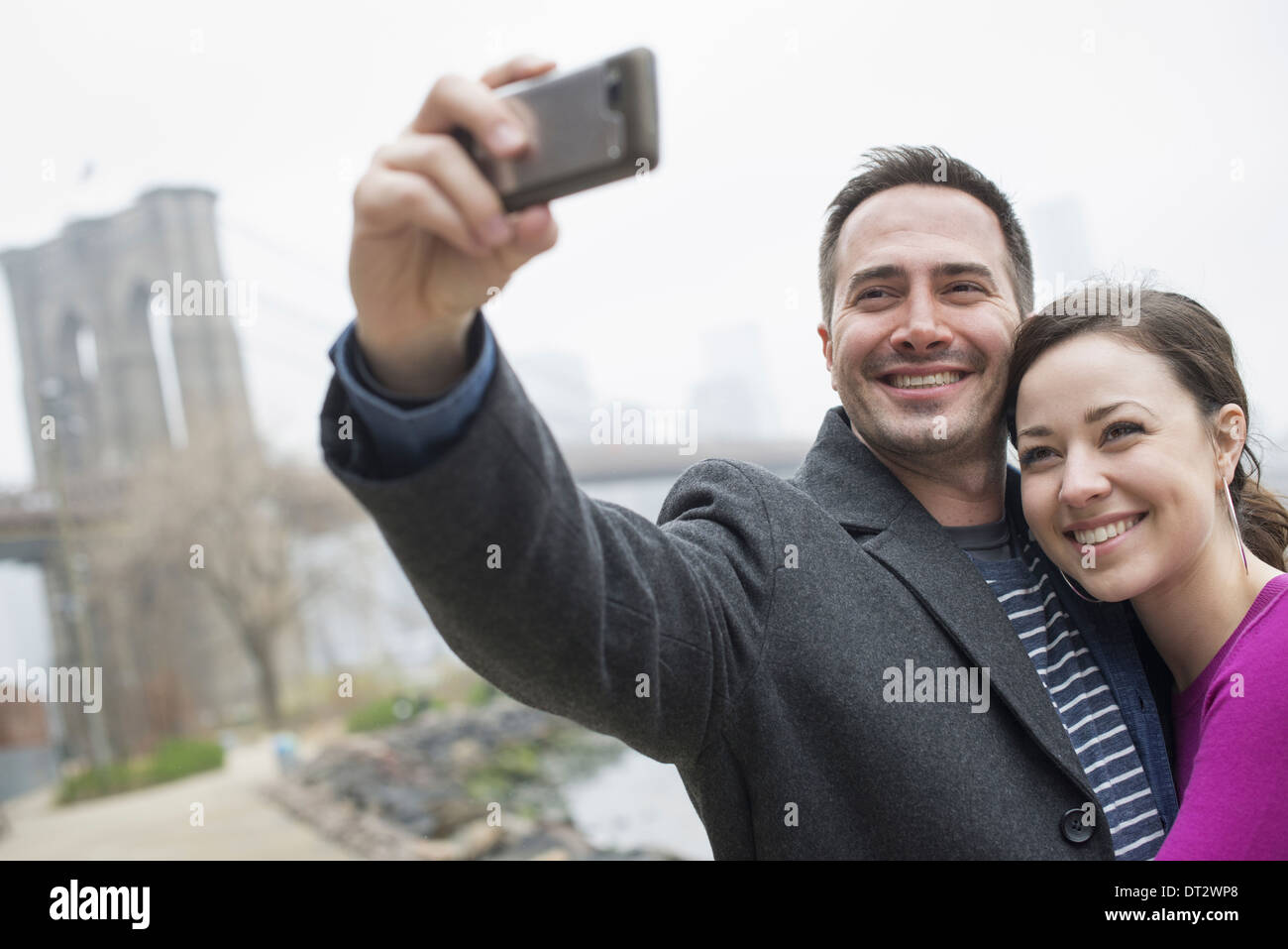 La città di New York il Ponte di Brooklyn attraversando il fiume est un paio di scattare una foto con un telefono un selfy di se stessi Foto Stock