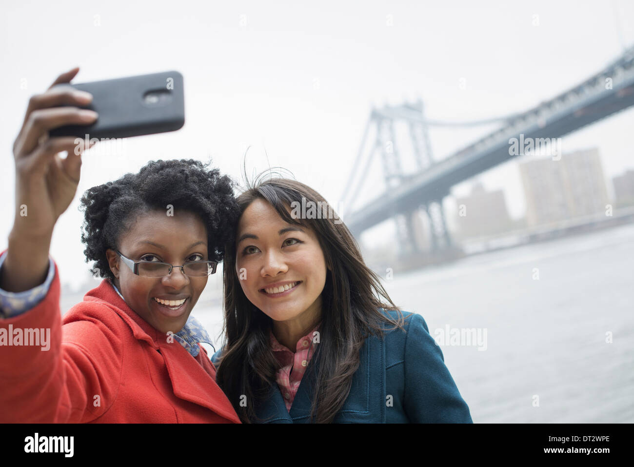 Il Ponte di Brooklyn attraversando il fiume est un paio di due donne di scattare una foto con un telefono un selfy di se stessi Foto Stock