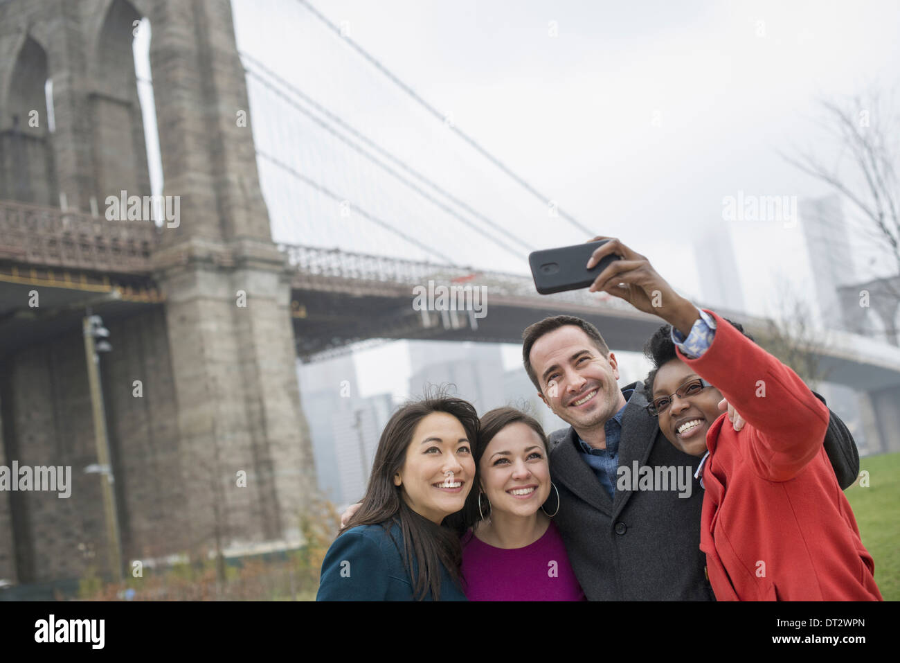 La città di New York il Ponte di Brooklyn attraversando la East River quattro amici di scattare una foto con un telefono un selfy di se stessi Foto Stock