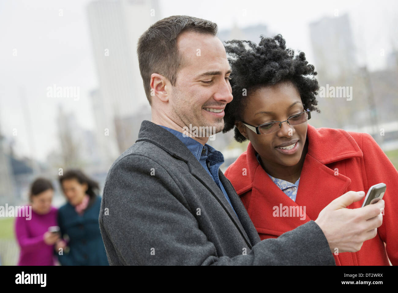 Un paesaggio urbano vista di Manhattan da Brooklyn quattro persone due in background e due controllando un telefono Foto Stock