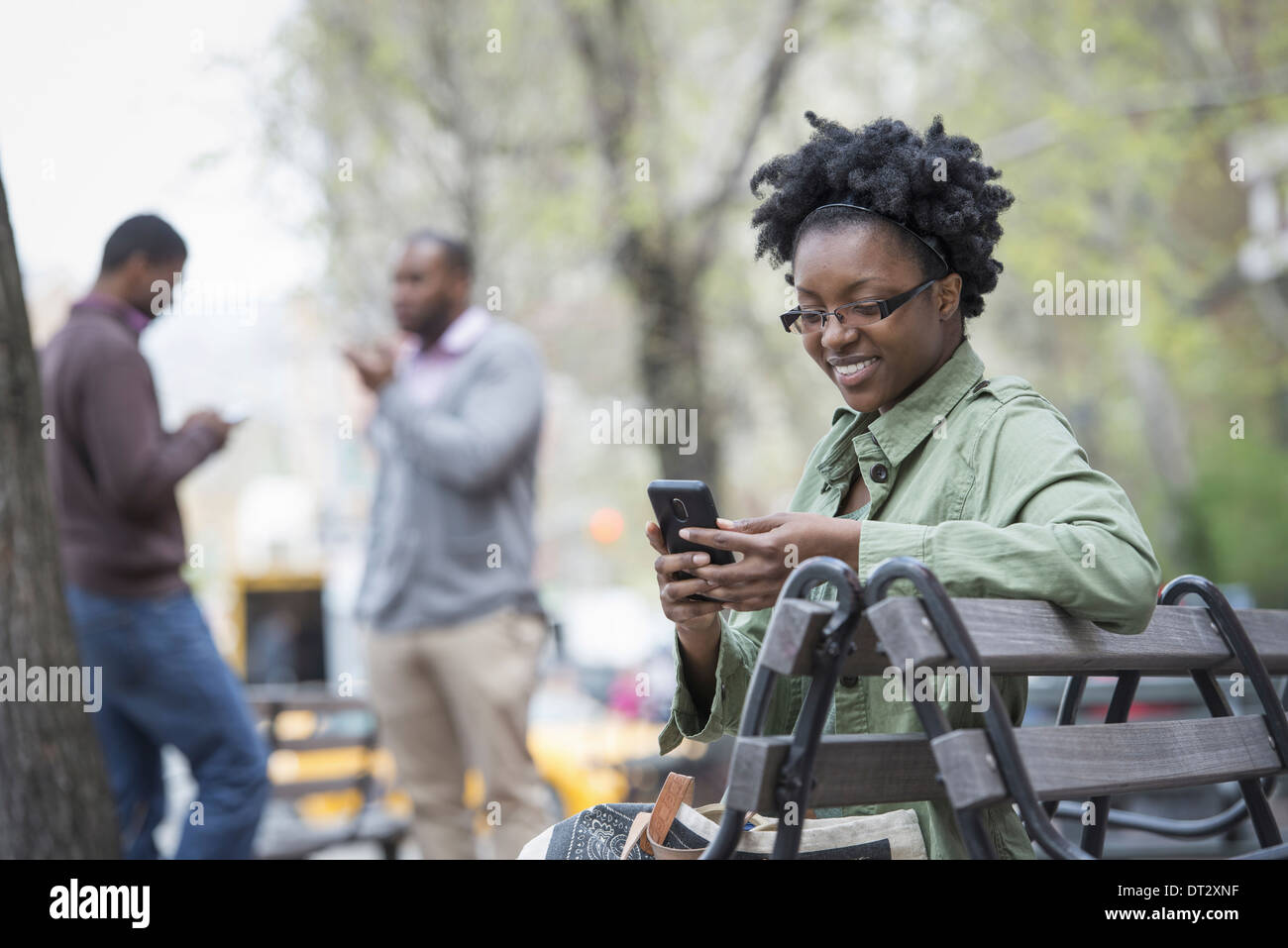 Una donna su un banco di controllo il suo telefono due uomini in background Foto Stock