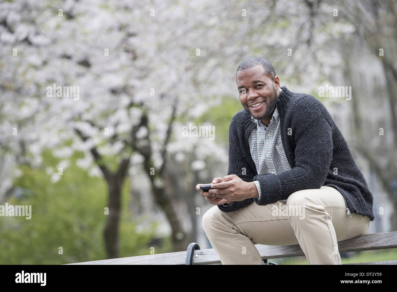 Un uomo seduto su una panchina nel parco in possesso di un telefono cellulare Foto Stock