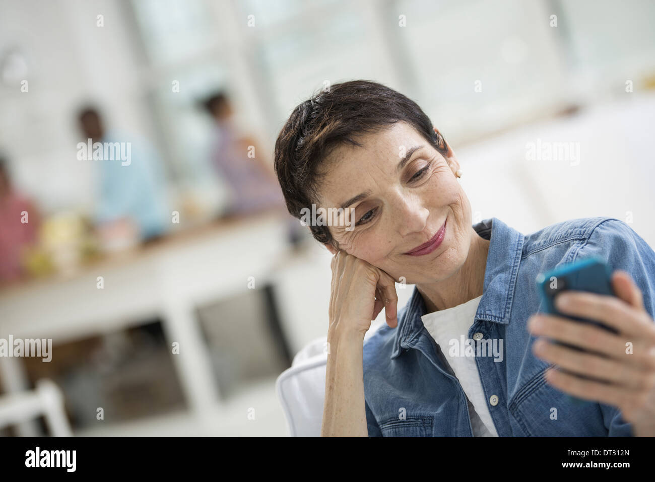 Una donna matura con i capelli grigi che indossa una maglietta denim guardando lo schermo di un telefono intelligente Foto Stock