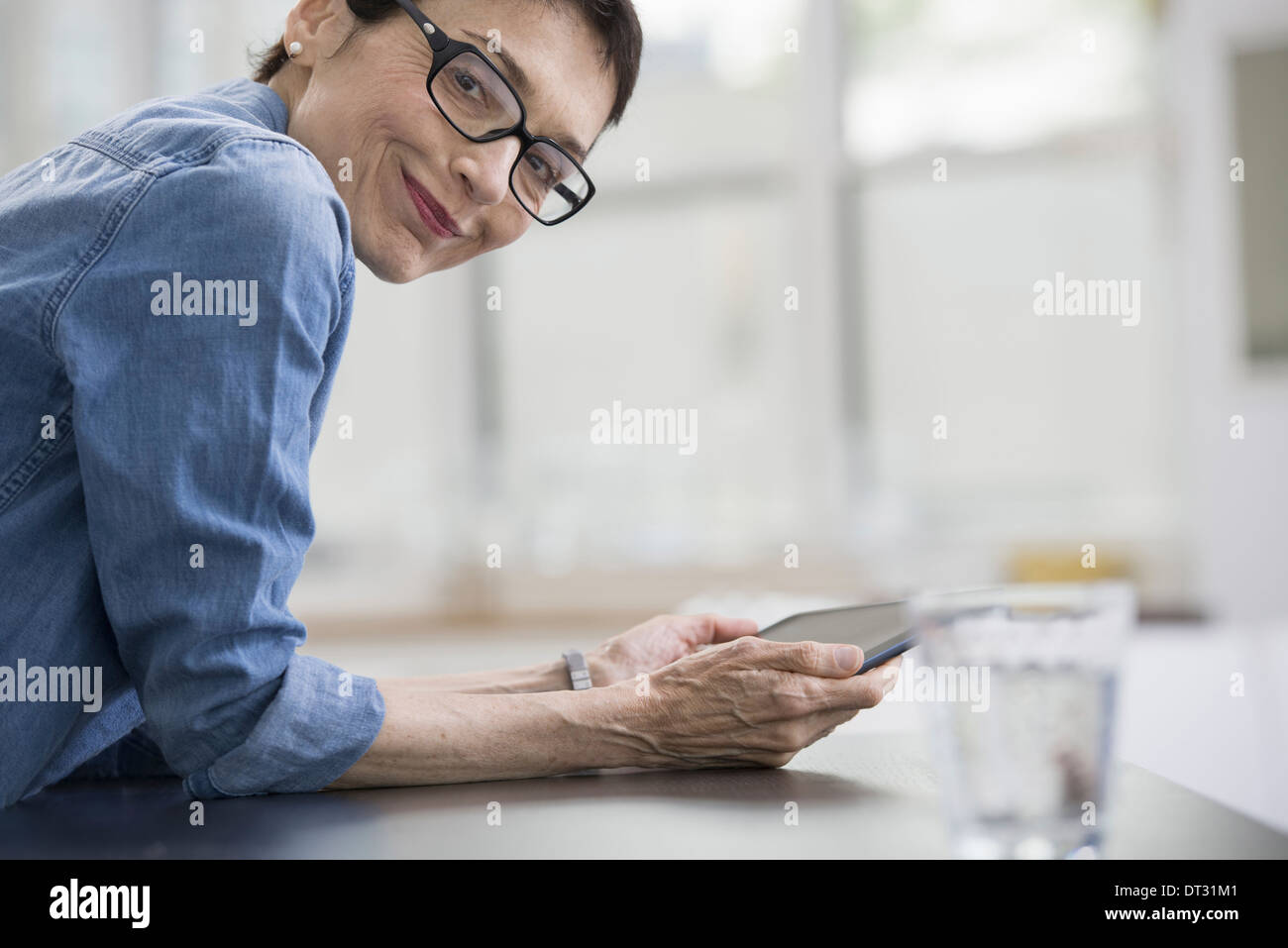 Professionisti in ufficio una luminosa e ariosa e luogo di lavoro di una donna matura in un blu denim shirt tenendo una tavoletta digitale Foto Stock