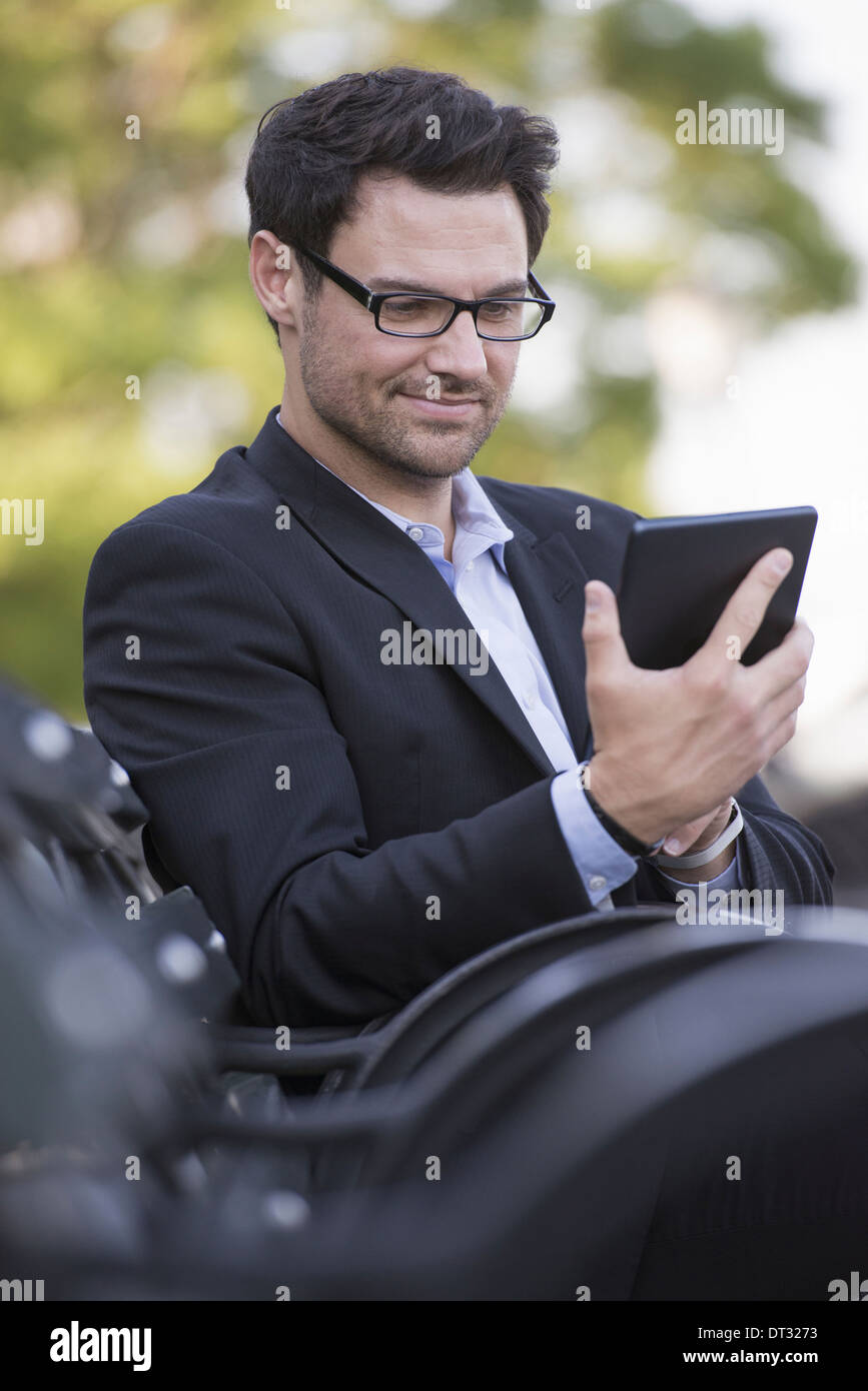 Un uomo seduto su una panchina utilizzando una tavoletta digitale Foto Stock