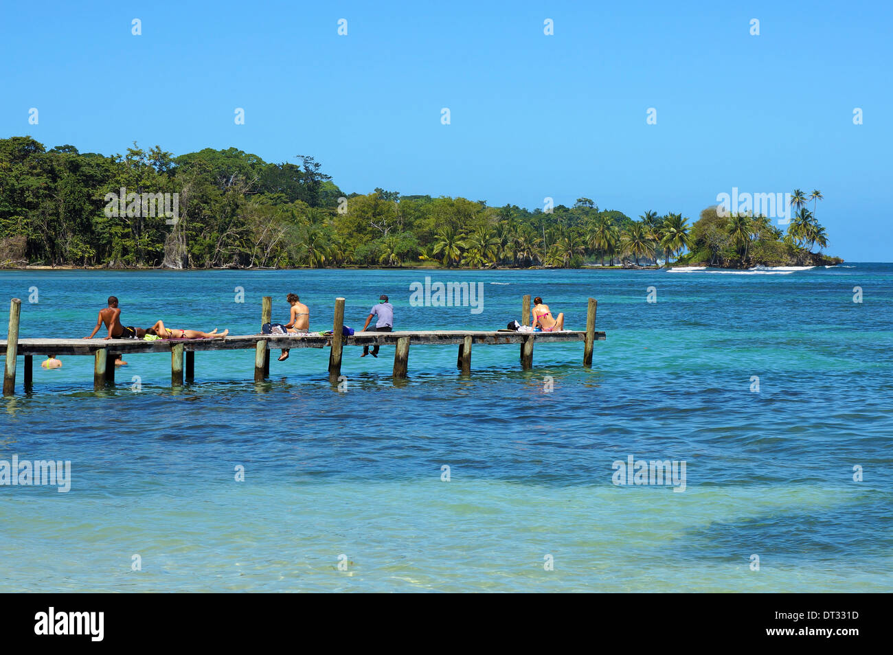 I turisti su un dock in legno sopra il Mar dei Caraibi e costa tropicale con vegetazione lussureggiante in background, Bocas del Toro, Panama Foto Stock