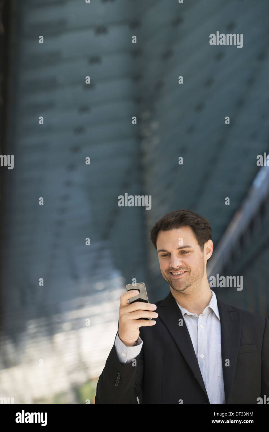 Un uomo in giacca nera e aprire la maglietta con spallamento utilizzando una smart phone Foto Stock