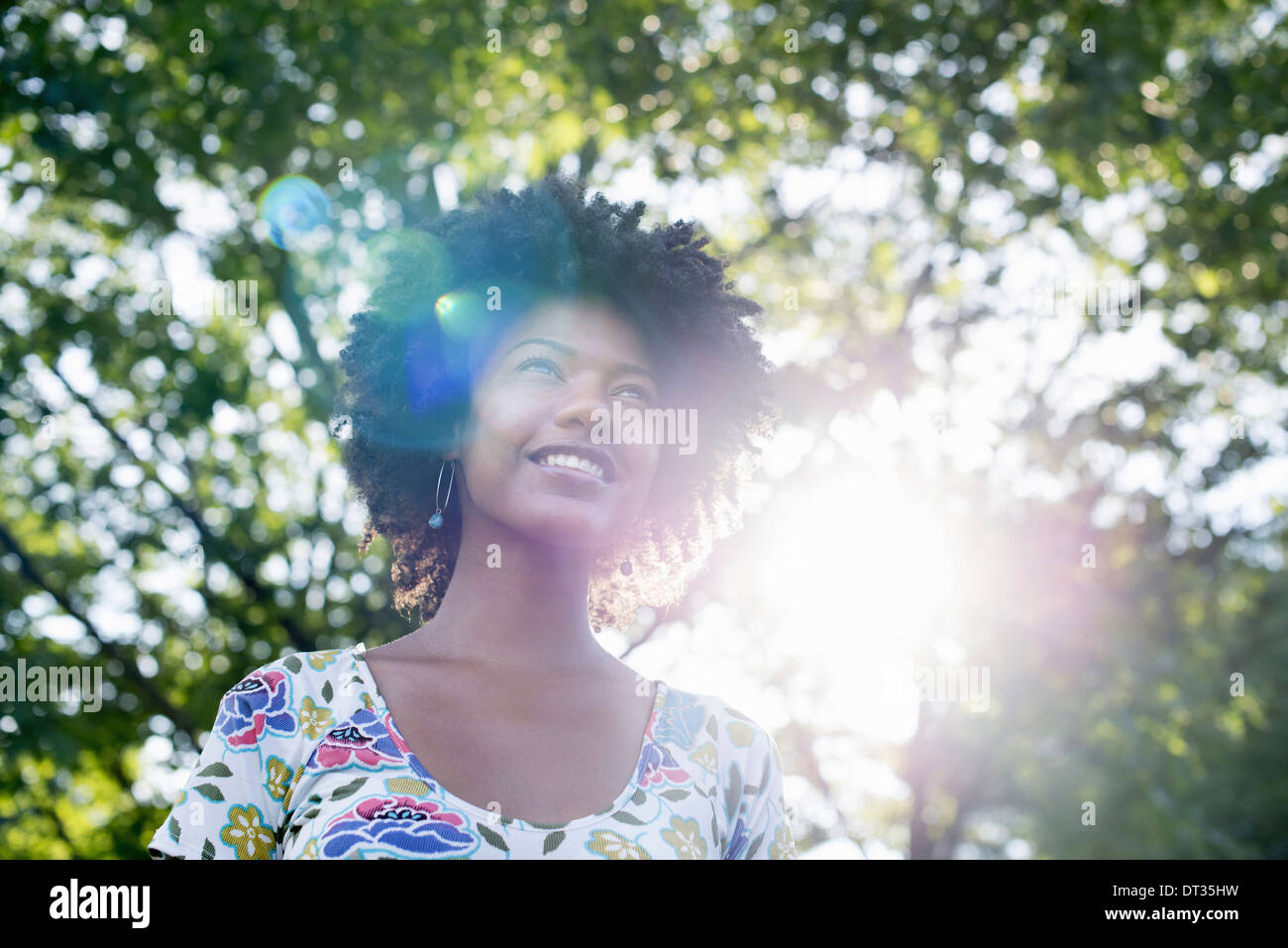 Una giovane donna in un fiorito abiti estivi con le mani dietro la testa sorridente e guardando in alto Foto Stock