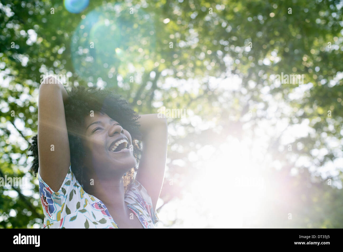 Una giovane donna in un fiorito abiti estivi con le mani dietro la testa sorridente e guardando in alto Foto Stock