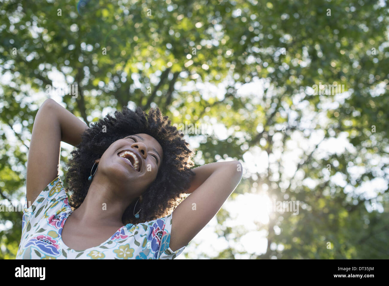 Una giovane donna in un fiorito abiti estivi con le mani dietro la testa sorridente e guardando in alto Foto Stock