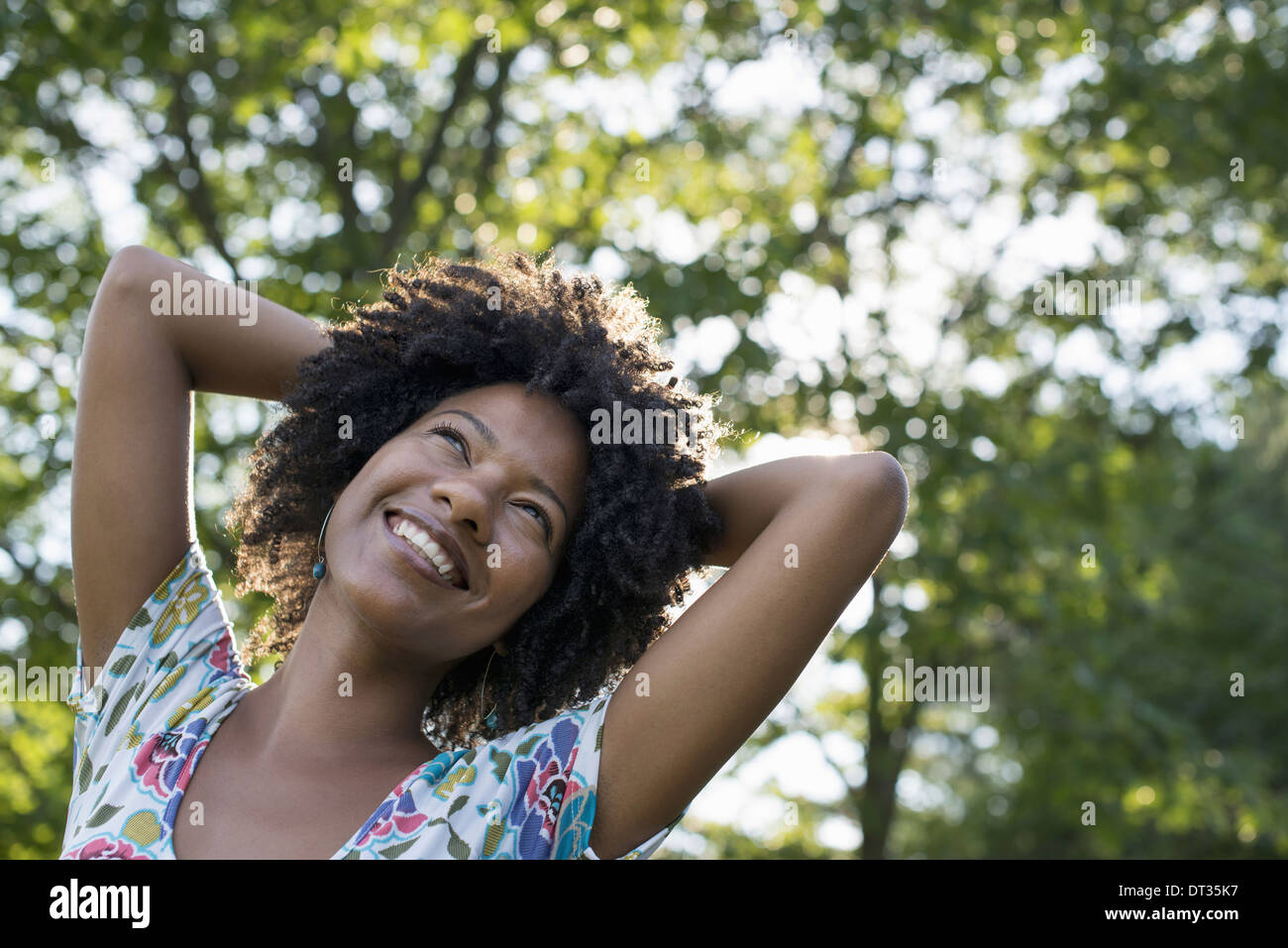 Una giovane donna in un fiorito abiti estivi con le mani dietro la testa sorridente e guardando in alto Foto Stock