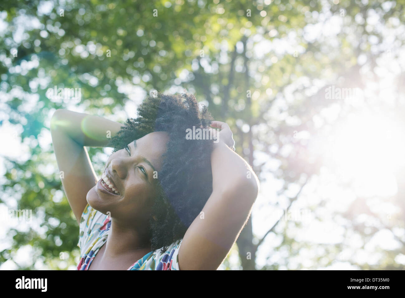 Una giovane donna in un fiorito abiti estivi con le mani dietro la testa sorridente e guardando in alto Foto Stock