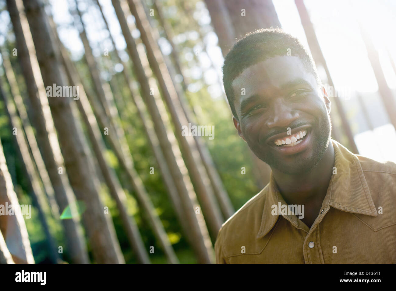 Un uomo sorridente con la videocamera sotto l'ombra degli alberi in estate Foto Stock
