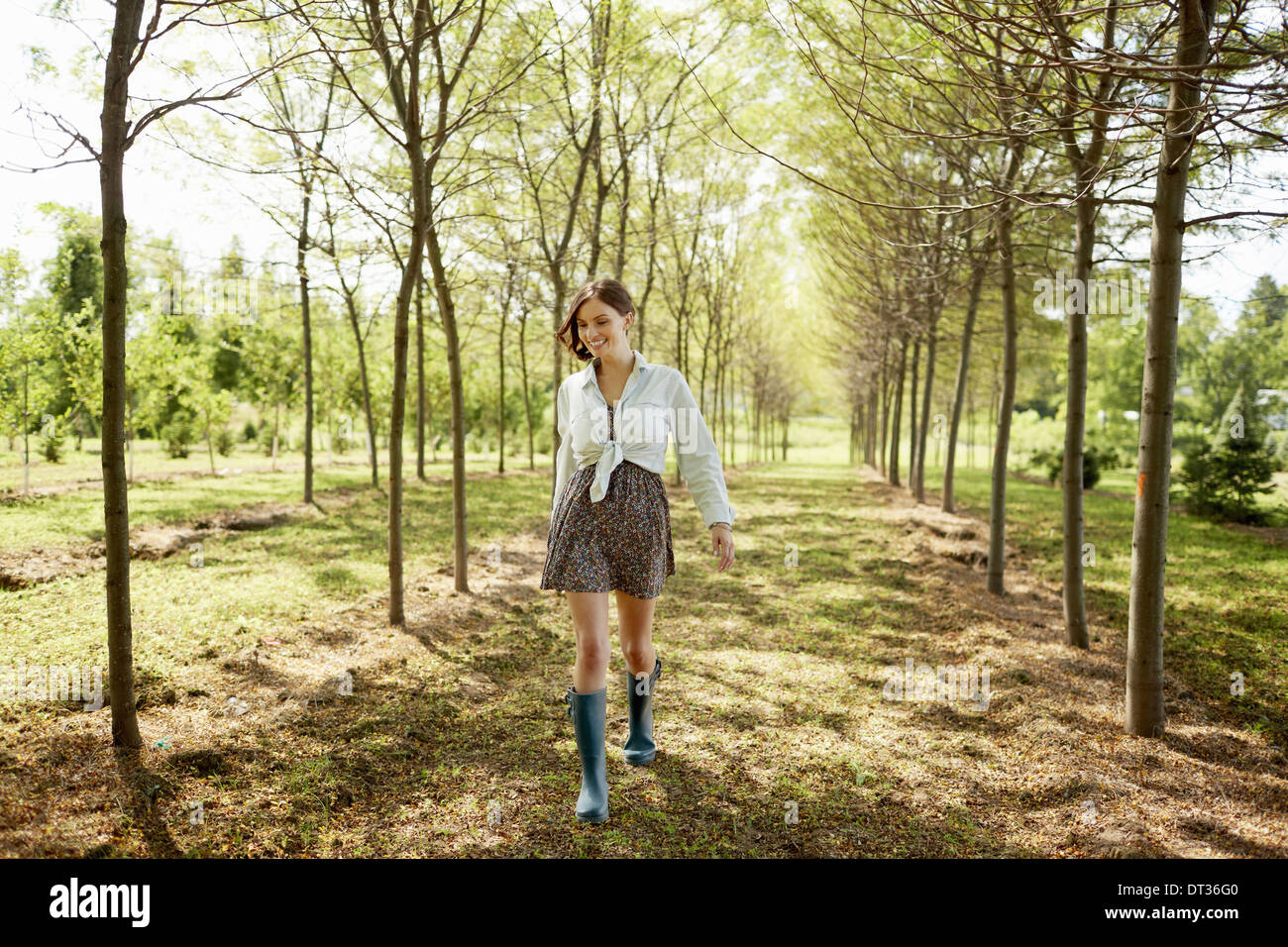 Una giovane donna che cammina verso il basso di un viale di alberi nel bosco Foto Stock