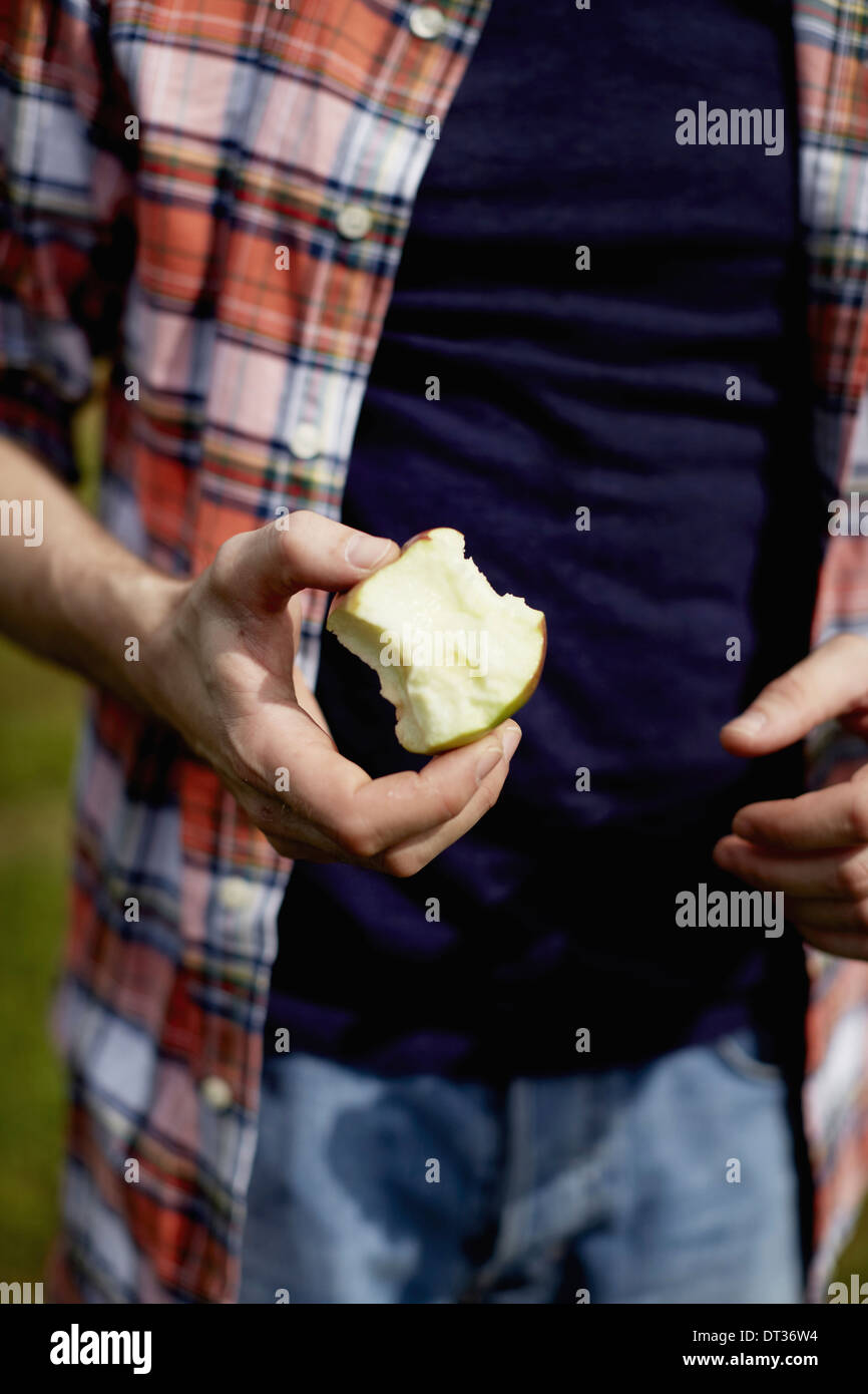 La sezione centrale di un uomo che indossa una camicia a quadri in possesso di una metà mangiato apple Foto Stock