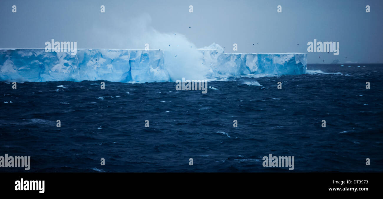 Un iceberg con ripidi fianchi, galleggia sull'acqua. Onde e salita a spruzzo. Evento del parto. Foto Stock