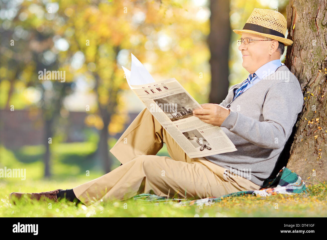 Senior gentleman seduto su un'erba leggendo il giornale in un parco in autunno Foto Stock