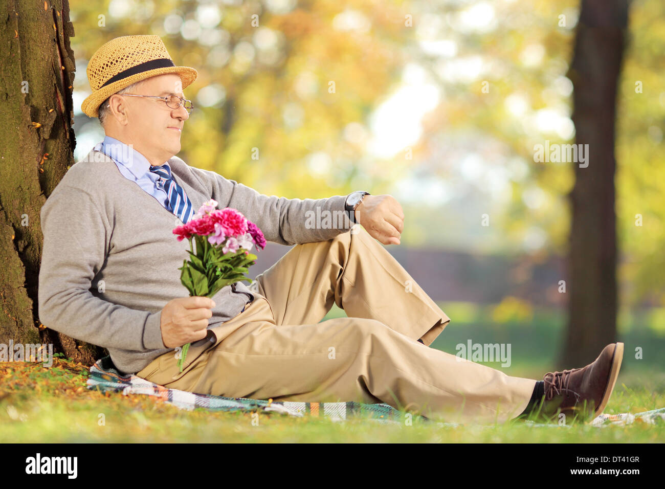Senior gentleman con fiori seduti su un prato verde e controllando il tempo in un parco Foto Stock