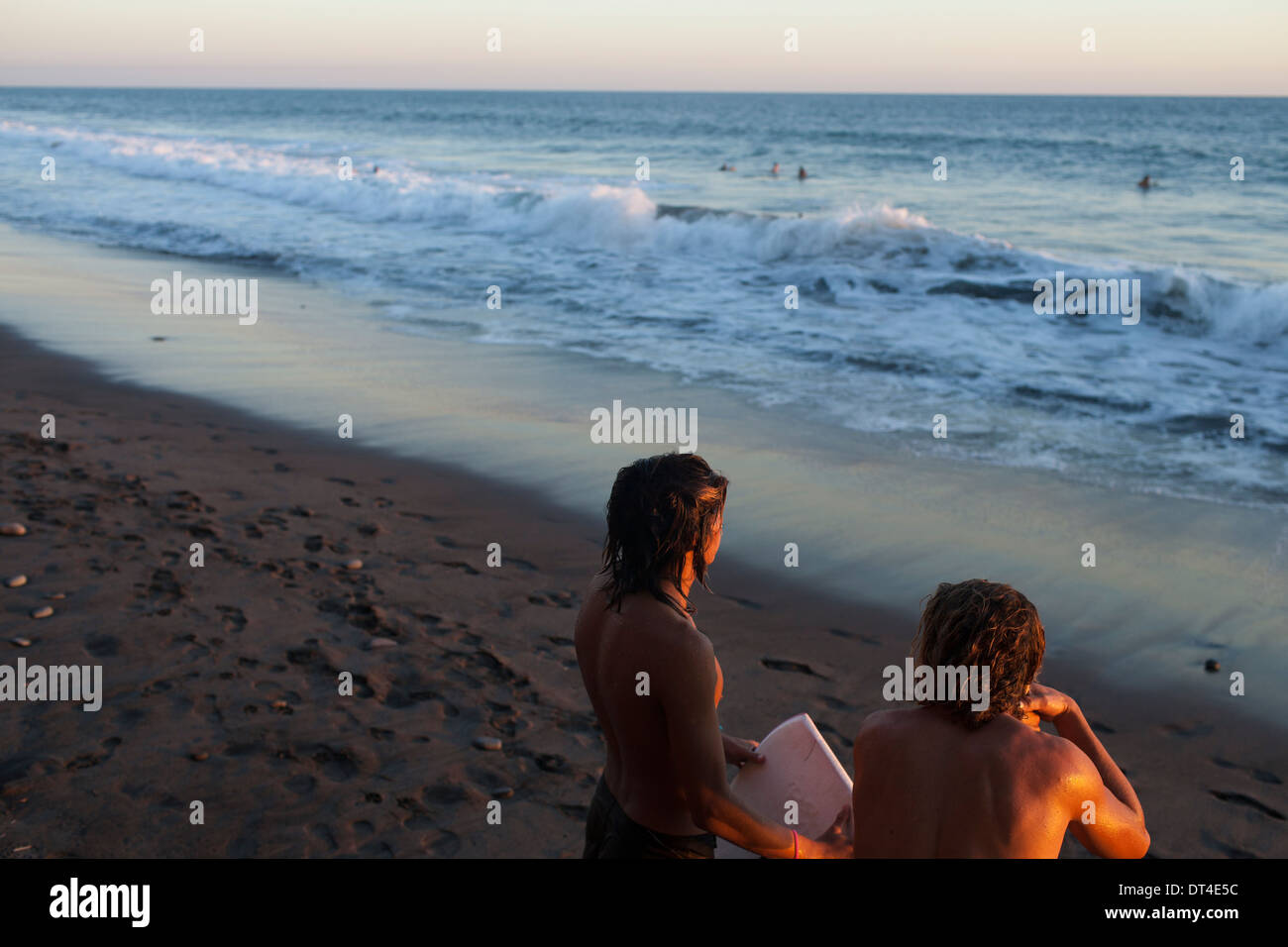 Due locale surf ragazzi cercare onde al tramonto sulla spiaggia di El Tunco, una cittadina balneare in El Salvador popolare tra i surfisti. Foto Stock