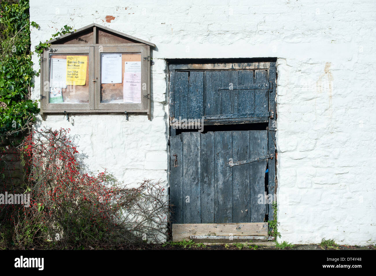 Nero antico stabile in legno porta accanto ad un villaggio bacheca su un dipinto di bianco muro di pietra nelle zone rurali di South Gloucestershire Foto Stock