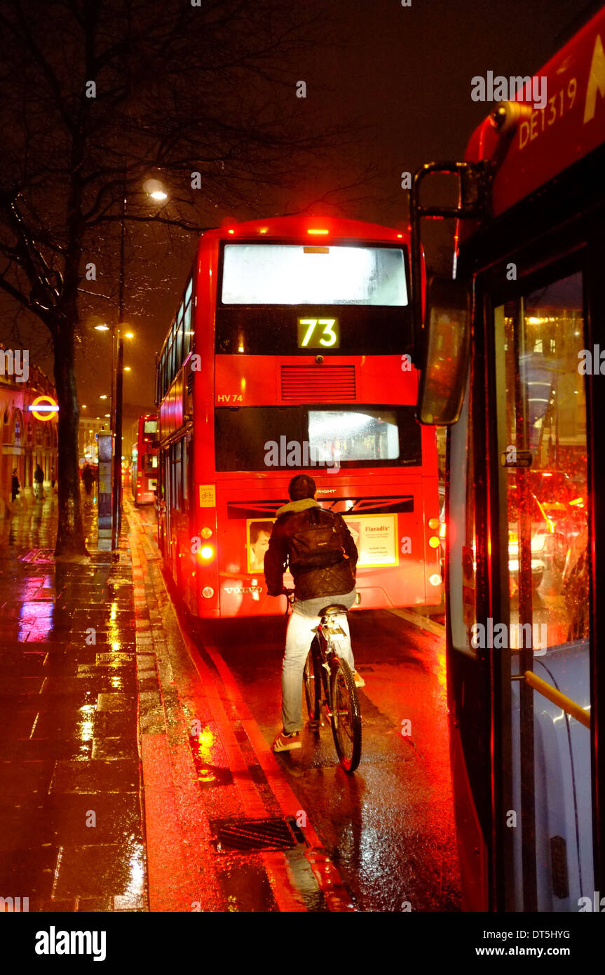 Ciclista tra autobus rossi di Londra durante la pioggia durante la notte Foto Stock