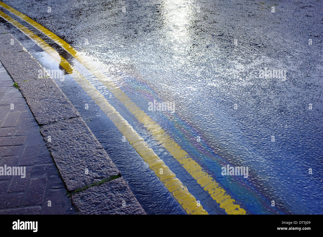 Doppia linea gialla sulla strada bagnata con marea nera la formazione di pattern arcobaleno Foto Stock