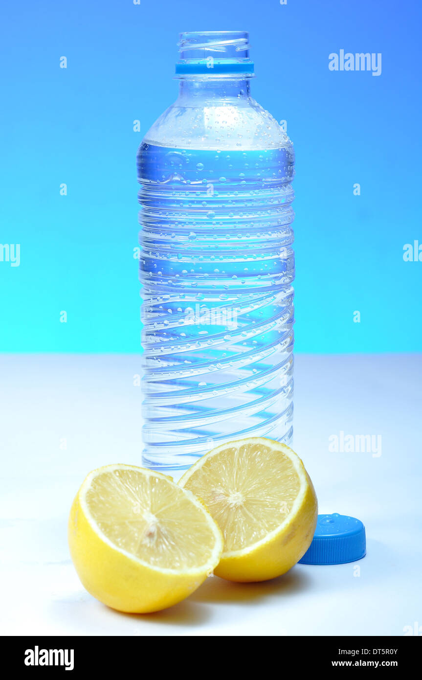 Bottiglia di acqua e limone contro sfondo blu Foto Stock