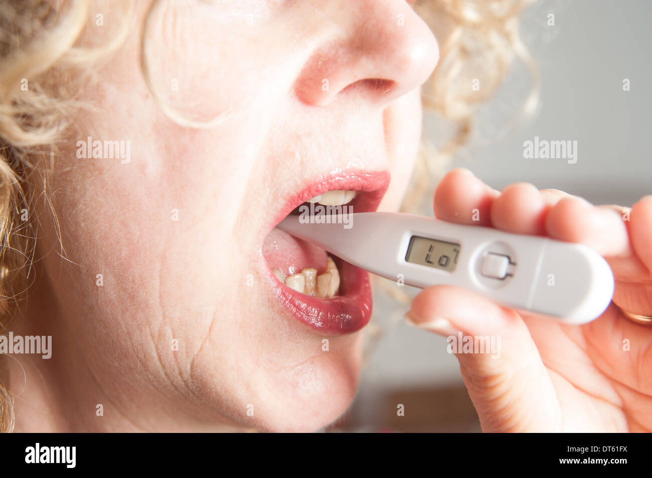 Donna prendendo la propria temperatura usando un termometro digitale Foto Stock