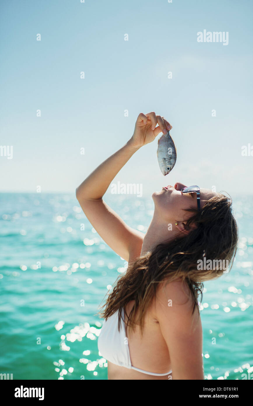 Giovane donna tenendo il pesce al di sopra della bocca, Islamorada, Florida Keys, STATI UNITI D'AMERICA Foto Stock