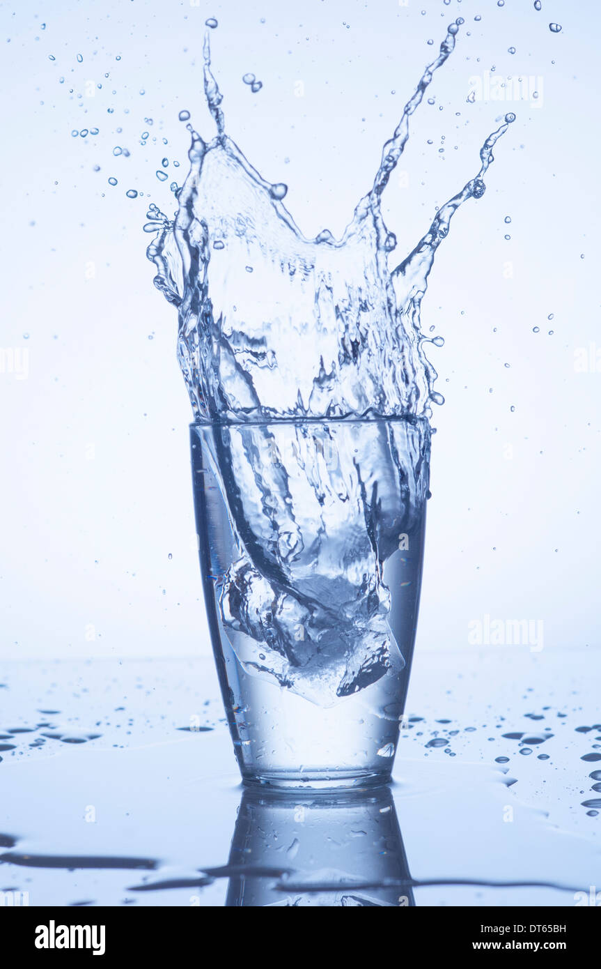 Schizzi di acqua in vetro con gocce su sfondo chiaro Foto Stock