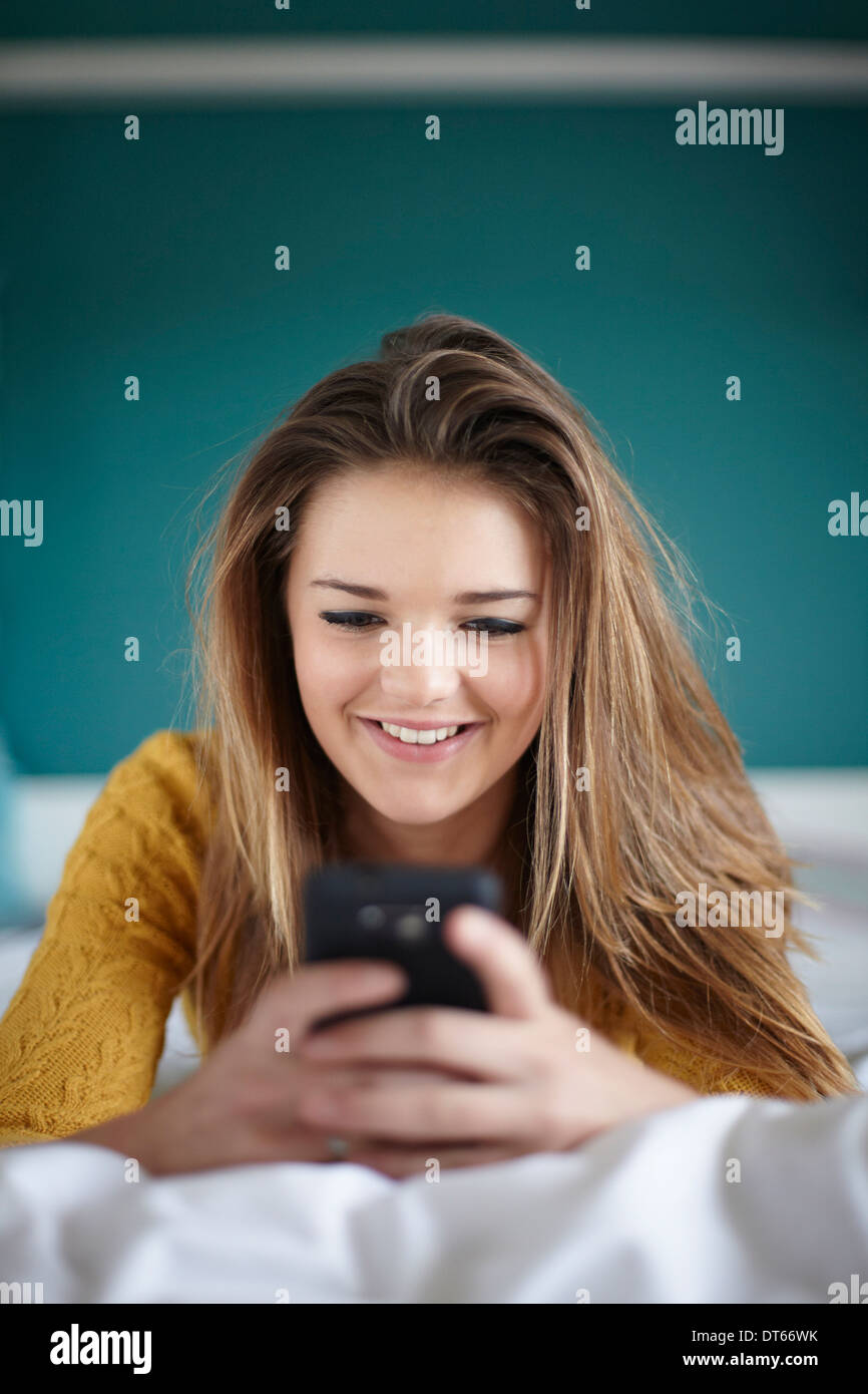 Ragazza adolescente in camera da letto i messaggi di testo sullo smartphone Foto Stock