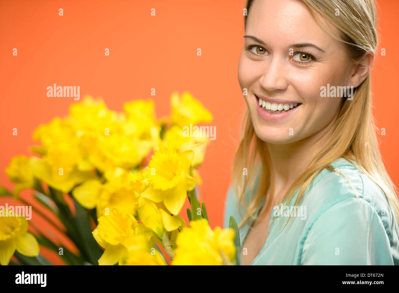 Donna sorridente con molla giallo fiori di narciso su sfondo arancione Foto Stock