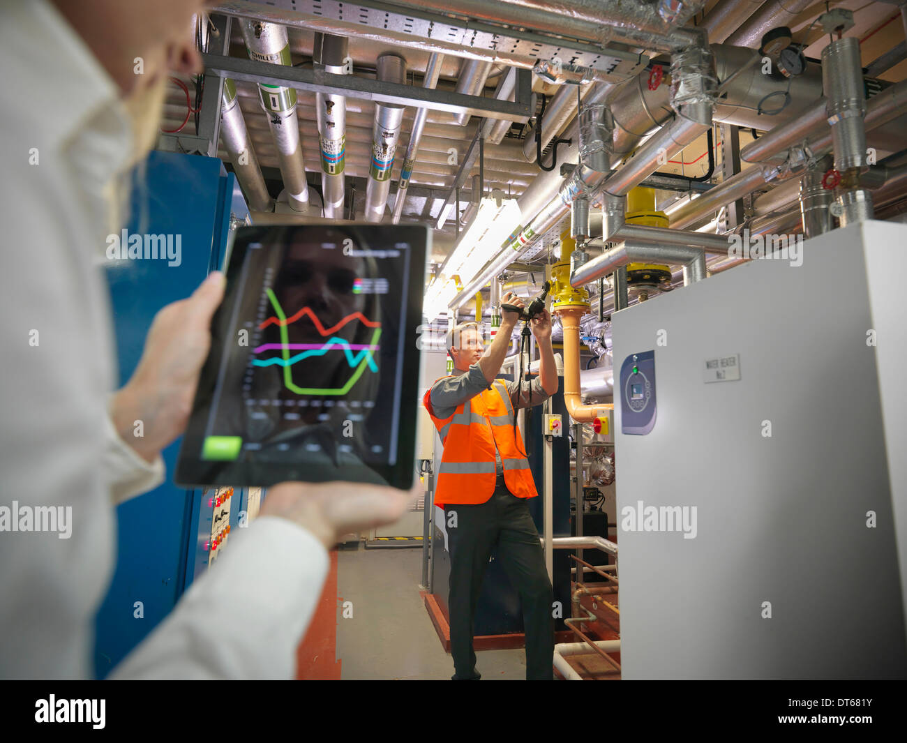 Gli impiegati utilizzano tavoletta digitale e fotocamera per controllare il rendimento di riscaldamento dell'ufficio nella camera di caldaia Foto Stock
